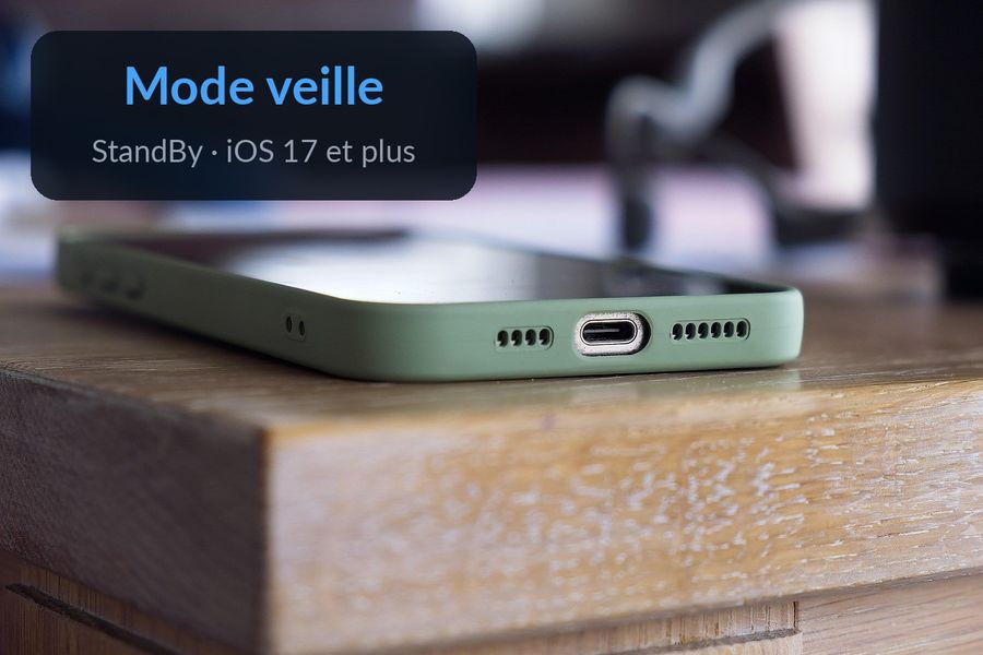 Un iPhone posé à l'horizontale en charge sur une table de chevet, avec les mots « Mode veille » et « StandBy » écrits dans le fond flou