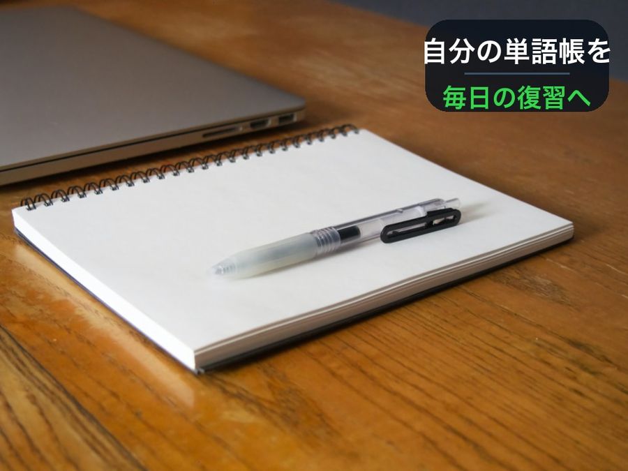 A notebook and pen on a desk, with a card reading 自分の単語帳を (your own vocabulary list) and 毎日の復習へ (into daily review) drawn into the empty wall behind it
