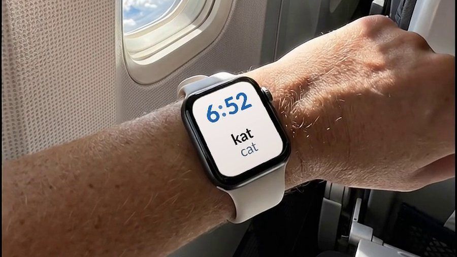 An Apple Watch on a plane, showing a Danish word and its English translation on the watch face