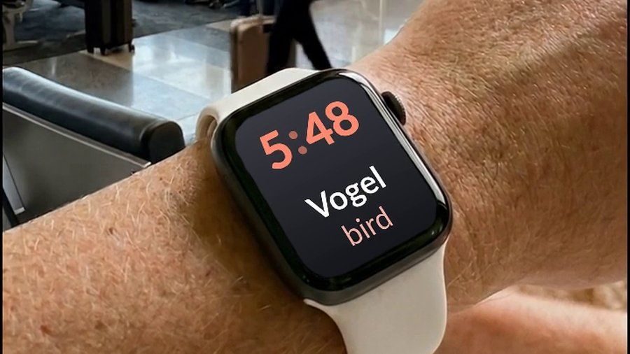 An Apple Watch at an airport, showing a German word and its English translation on the watch face