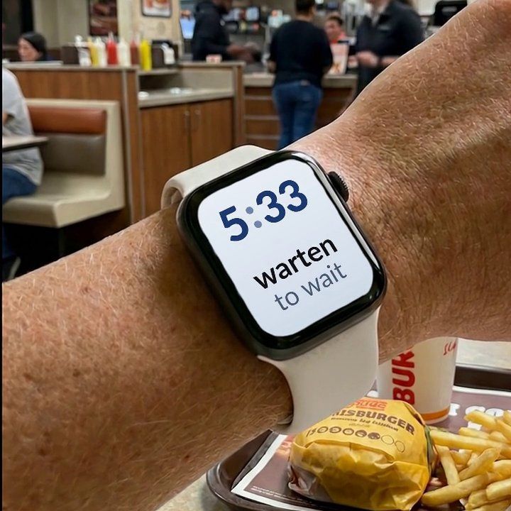 An Apple Watch in a fast-food restaurant, showing a German word and its English translation on the watch face