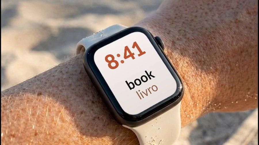 Um Apple Watch no pulso em uma praia, mostrando a palavra em inglês book e sua tradução em português, livro, abaixo do horário