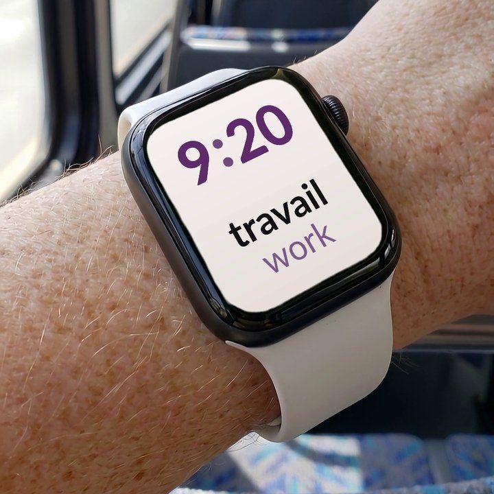 An Apple Watch on a wrist in a bus, showing the French word travail and its English translation, work, under the time