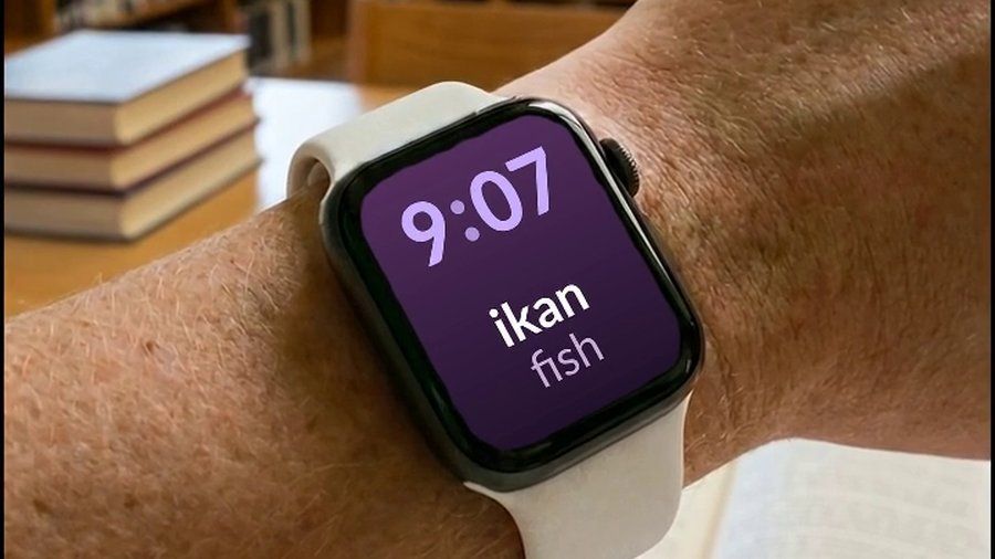 An Apple Watch in a library, showing a Indonesian word and its English translation on the watch face