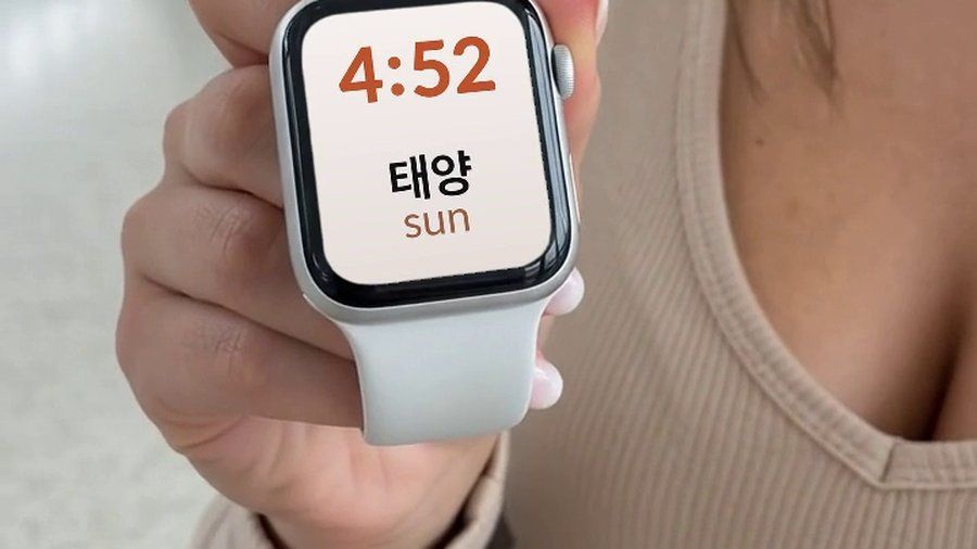 An Apple Watch held in the hand, showing a Korean word and its English translation on the watch face