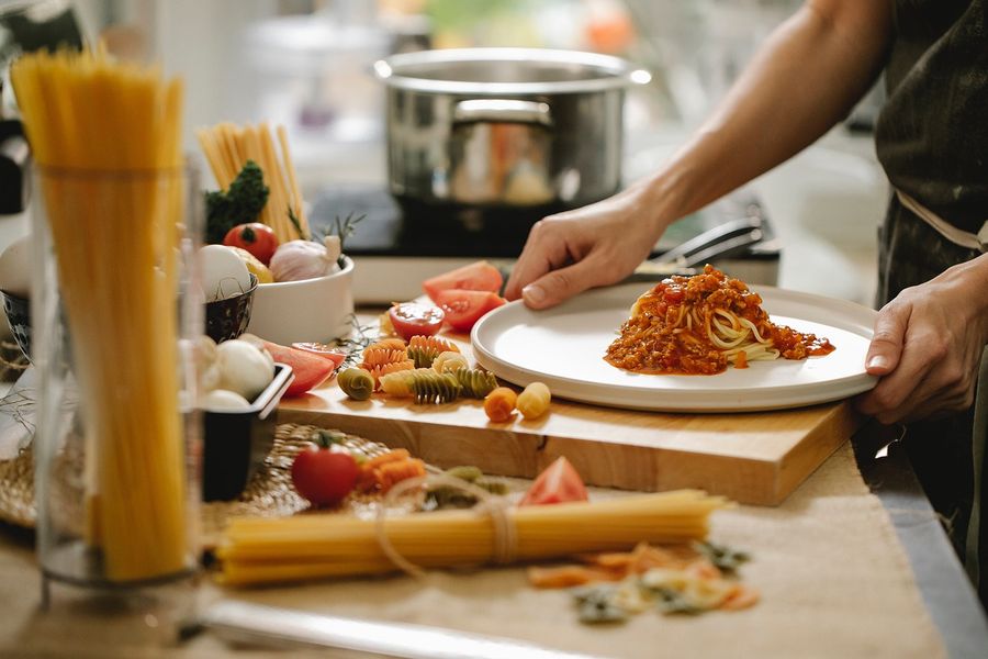 A cook plating pasta with tomato sauce in a kitchen