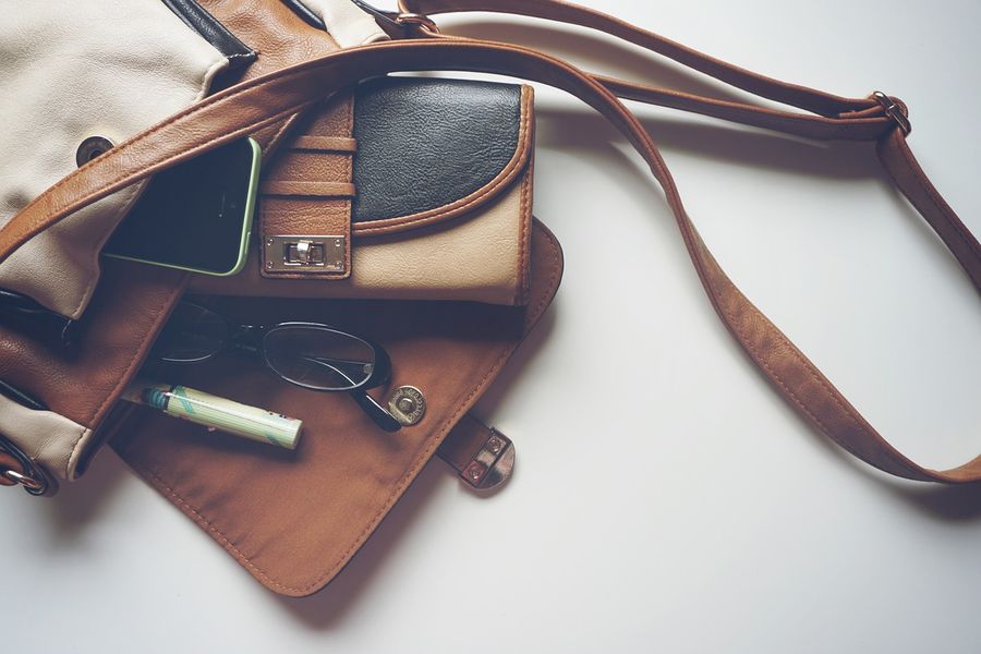 A handbag with a phone, glasses and lip balm lying beside it