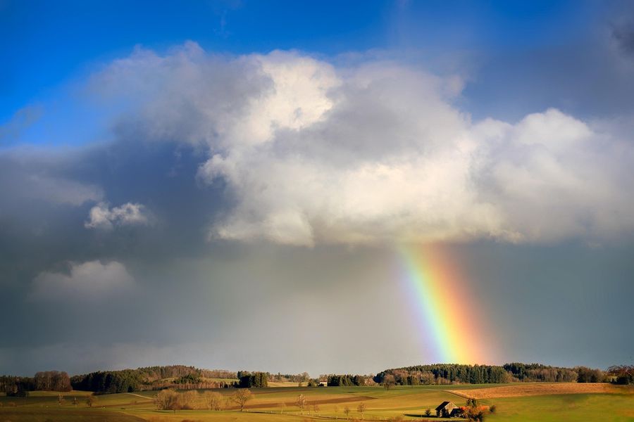 A rainbow over fields beneath a cloudy sky